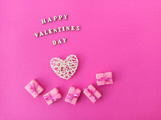 On a pink background, congratulations made of wooden letters, small gifts with a bow and a heart. Valentine's Day greeting card. 