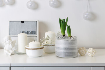 Unblown hyacinths with burning candles on a tray, a stack of books, a mug of tea, a garland of thread on the wall. Easter room decoration.