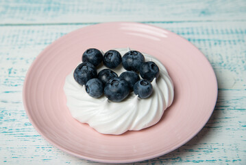 Pavlova cake with blueberries and mint on a pink platter. Home confectionery. Old retro white and blue table.