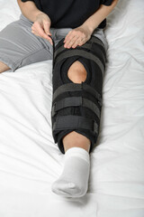 Woman fixing adjustable Velcro orthosis on broken leg sitting in bed. Wearing leg brace after injury. Closeup. Vertical orientation.