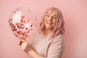 Beautiful young attractive girl with a transparent colored balloon, having fun enjoying the holidays in a pink background