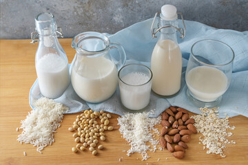 Various vegan milk alternatives from rice, soy, coconut, almond and oats in bottles and glasses on a wooden table, selected focus