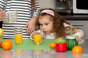 A little girl watches as orange juice is being prepared. Two cute sister girls are making orange fresh juice. They are in the kitchen at home. Family. Fresh fruit. Healthy eating.