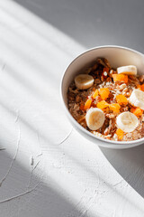 Delicious dietary healthy breakfast of oatmeal, dried fruits, nuts and bananas in a white bowl at sunny morning