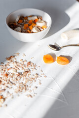 Delicious healthy breakfast of muesli with oatmeal, dried apricots, banana and nuts with a spoon on a white table at sunrise in the early morning. Raw vegan food at sunlight