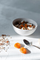 Delicious healthy breakfast muesli food with dried apricots and bananas in a white bowl on a white table early in the morning at sunrise
