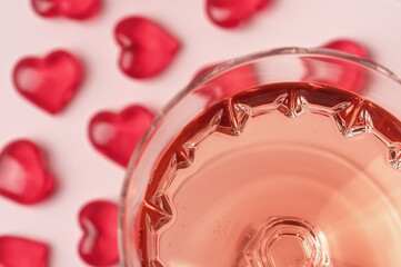 Crystal glass of rose sparkling wine or champagne and red glass hearts on pastel pink background. Shot with selective soft focus. Happy Valentines Day concept.