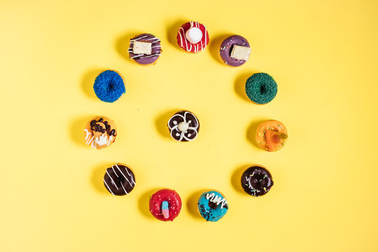 Colorful donuts or doughnuts in various shapes on yellow bright background. Colorful and happy image and concept.