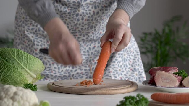 Preparation of beef broth or soup - scraping carrots, with marrow bones, meat and vegetables in the background