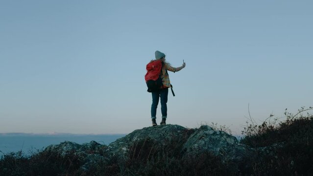 Cinematic shot of beautiful young woman on top of mountain peak film record video or make photos of sunset and landscape scenery. Concept adventure travel blogger. Outdoors living lifestyle