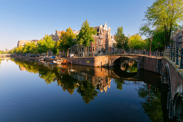 Old canal houses along the intersection of Keizersgracht and Reguliersgracht canals in Amsterdam on a calm sunny morning.