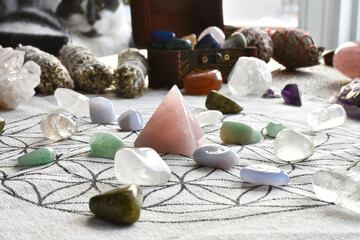 A close up image of a sacred crystal healing grid with white sage smudge sticks and a black and...