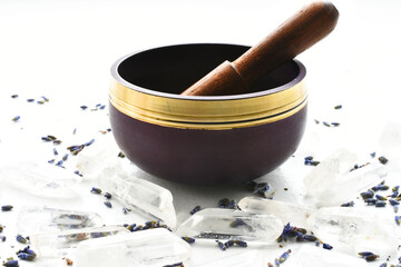 A side view image of a purple meditation singing bowl and wooden mallet with clear quartz crystals and dried lavender flowers. 