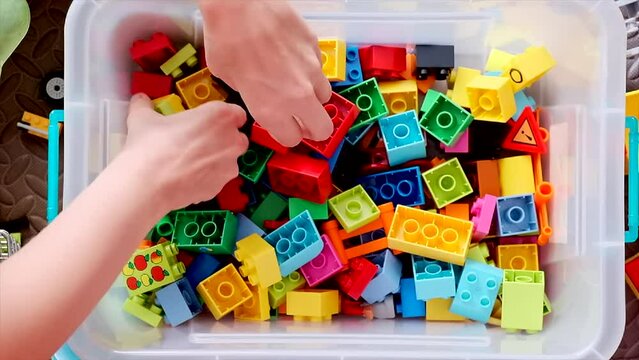 Overhead shot of a woman's hands in a box of building blocks sorting them.