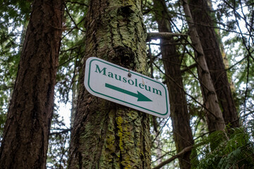 Angled view of a directional arrow sign, pointing the direction to a mausoleum deep in a forested...