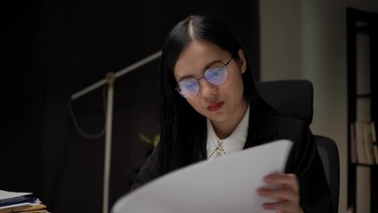 Young asian business woman working at late night. She was very busy checking paperwork and had to send the work before the deadline, feeling stressed. Sitting in the dark office at night.