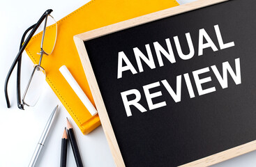 ANNUAL REVIEW text on the blackboard with notepad , pen, pencil