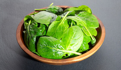 Spinach leaves in a wooden plate on a black background Top view.
