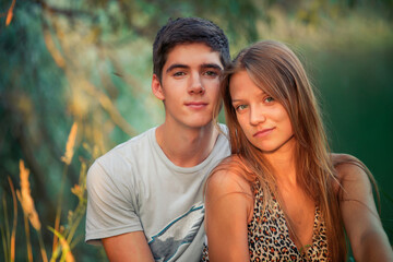 Obraz premium Loving and happy guy and girl are sitting on the lake in the forest. Lovers in an embrace celebrating Valentine's Day.