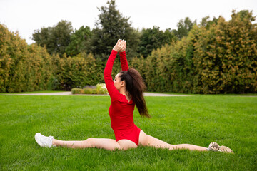 Beautiful girl athlete in red bodysuit training in the park