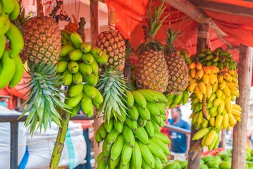 Fotobehang Bananas and pineapples hang under the roof of street shop in Zanzibar, Tanzania. © garrykillian