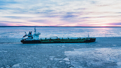 Enormous cargo ship sailing through ocean water with thick layer of broken ice pieces covering...