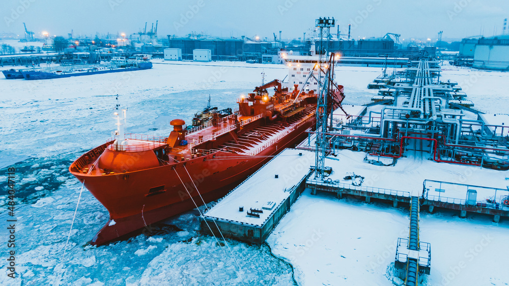 Wall mural northern oil terminal in snow and tanker illuminated by red lights moored on ocean water covered wit