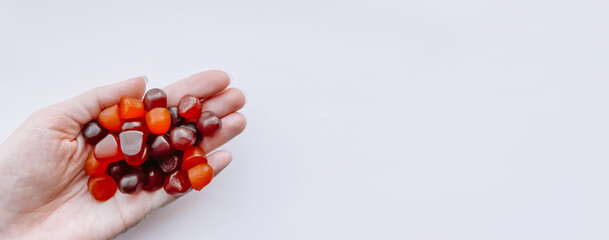 Group of red, orange and purple multivitamin gummies in the hand isolated on white background - obrazy, fototapety, plakaty
