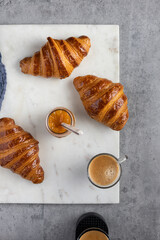 Overhead view of three glittering homemade croissants over a marble board with an orange marmalade jar in the middle.