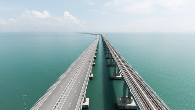 Aerial view along the long beautiful bridge above turquoise sea. Action. Flying above bending bridge with driving cars.