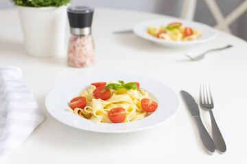 Italian pasta, pasta with cherry tomatoes and a sprig of basil in a white plate on a white table. Vegetarian food. Lunch or dinner at home. Healthy food.