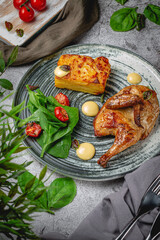 Fried tobacco chicken with lasagna, spinach and tomato in a plate on a gray stone table. Restaurant Menu