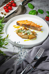 Salmon fillet baked with rustic potatoes on sweet pears stuffed with noble cheese with a sauce of ripe oranges in a plate on a gray stone table. Restaurant Menu