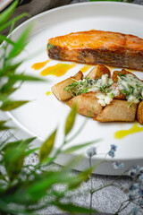 Salmon fillet baked with rustic potatoes on sweet pears stuffed with noble cheese with a sauce of ripe oranges in a plate on a gray stone table. Restaurant Menu