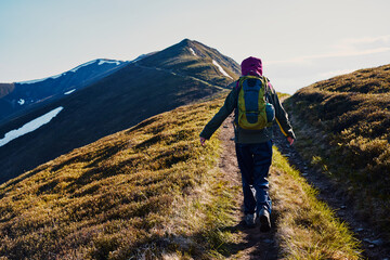 A woman walks along a mountain path along a mountain range. Rear view.