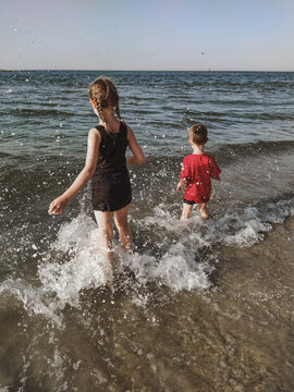 Two children have fun in the splashes of the sea on the shore