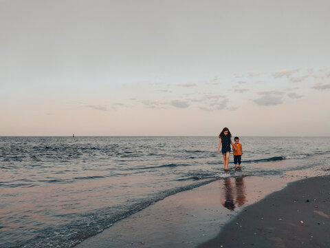 Two children walk along the seashore holding hands against the sky