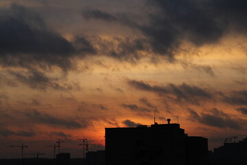 urban house and building cranes against the backdrop of a sunset sky with clouds