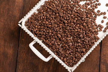 Coffee beans scattered on a white tray on rustic wood, Top view.