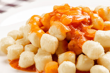 Potato gnocchi with sauce in detail on a white plate on a black and white checkered tablecloth, selective focus.