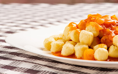 Potato gnocchi with sauce in detail on a white plate on a black and white checkered tablecloth, selective focus.