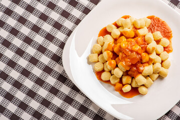 Potato gnocchi with sauce on a white plate on a black and white checkered tablecloth, Top view