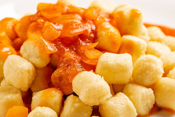 Potato gnocchi with sauce in detail on a white plate on a black and white checkered tablecloth, selective focus.
