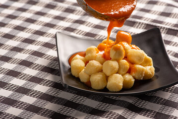 Potato gnocchi with sauce in detail on a black plate over a black and white checkered tablecloth, selective focus.