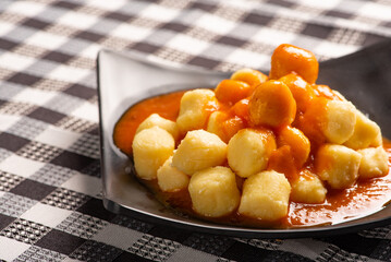 Potato gnocchi with sauce in detail on a black plate over a black and white checkered tablecloth, selective focus.