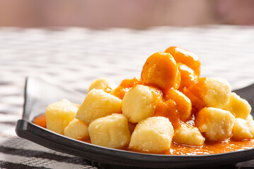Potato gnocchi with sauce in detail on a black plate over a black and white checkered tablecloth, selective focus.