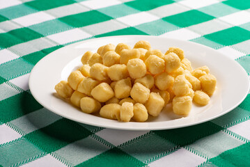 Potato gnocchi without sauce on a white plate on a green and white checkered tablecloth, selective focus.