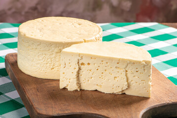 Semi-cured cheese from Brazil arranged on a rustic board on a green and white checkered tablecloth, selective focus.