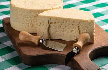 Semi-cured cheese from Brazil arranged on a rustic board on a green and white checkered tablecloth, selective focus.