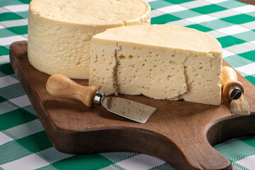 Semi-cured cheese from Brazil arranged on a rustic board on a green and white checkered tablecloth, selective focus.